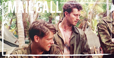 One U.S. Marine (circa WWII) sits in front of another, who is standing with his shirt open in the Pacific jungle.